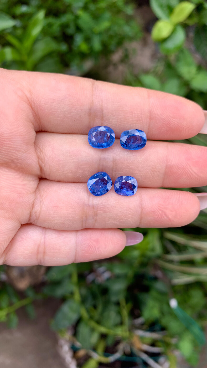 Four faceted cobalt blue spinels from Luc Yen held in the hand for scale