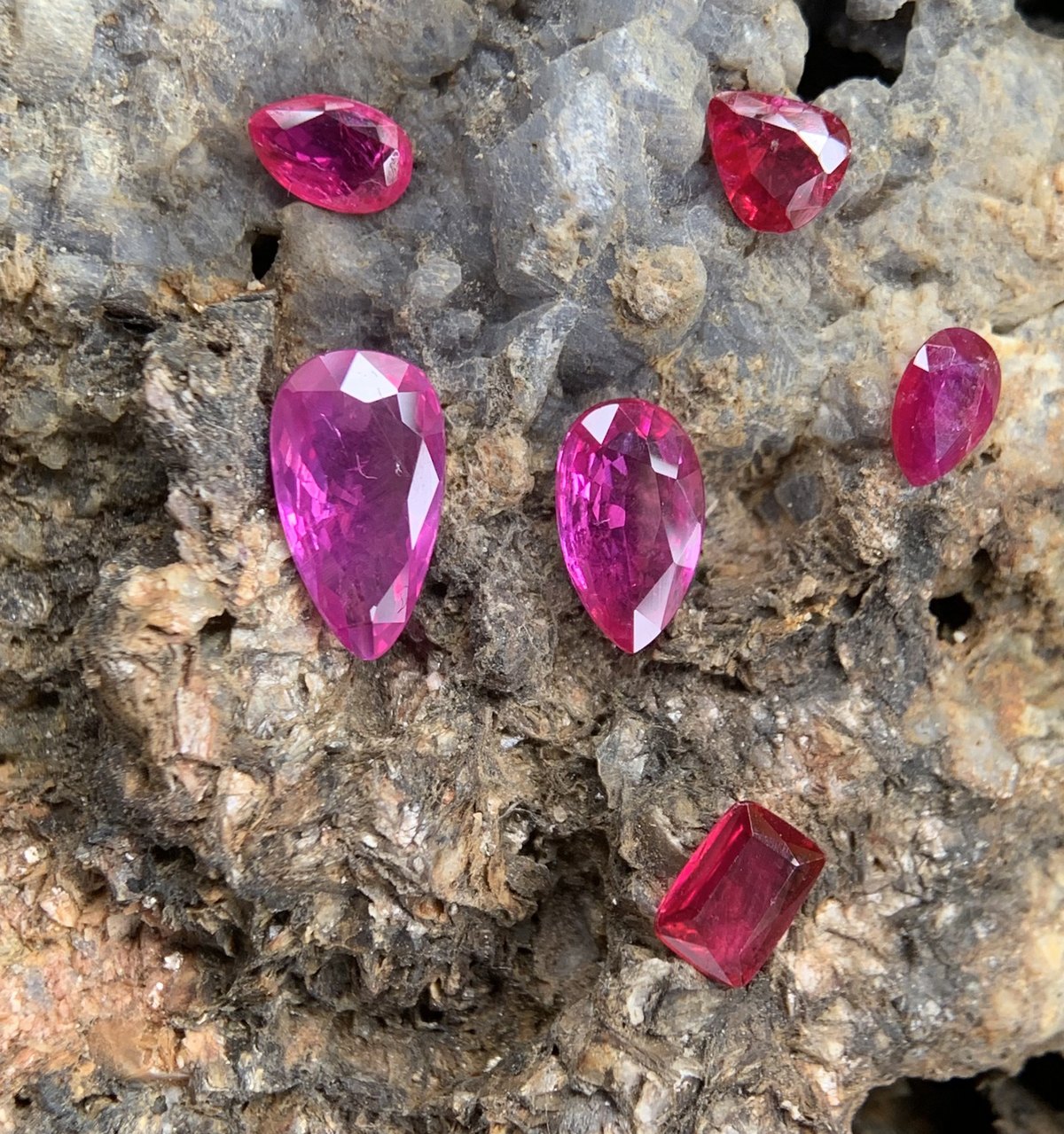 Six natural Luc Yen rubies laid on marble host rock, showing colour running from purplish pink through to vivid red