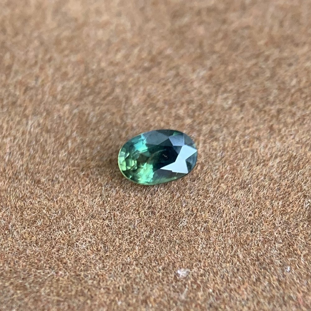 A small oval natural teal-green sapphire from Vietnam photographed on a neutral surface